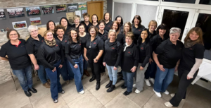 Eine Gruppe von Frauen in schwarzer Kleidung steht in einem Raum und schaut nach links oben in die Kamera