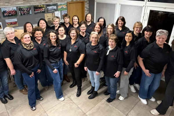 Eine Gruppe von Frauen in schwarzer Kleidung steht in einem Raum und schaut nach links oben in die Kamera